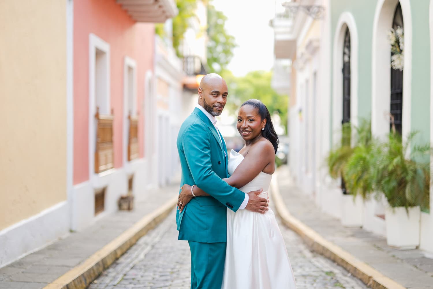 Couple standing in front of a colorful wall on a cobblestone street during their intimate destination wedding photoshoot in Old San Juan.