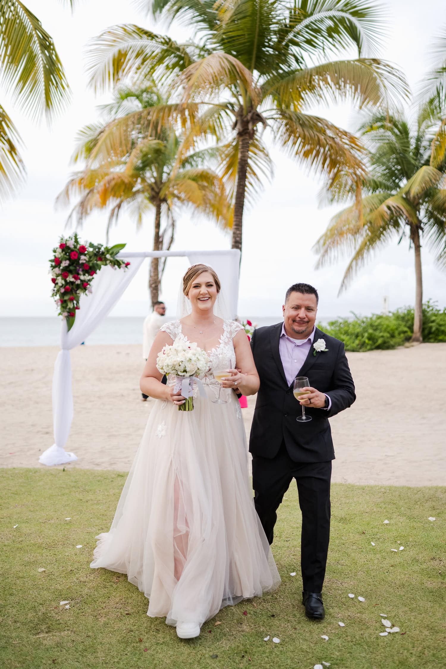 Beachfront wedding ceremony setup with a floral arch and palm trees at Courtyard Marriott Isla Verde, Puerto Rico.