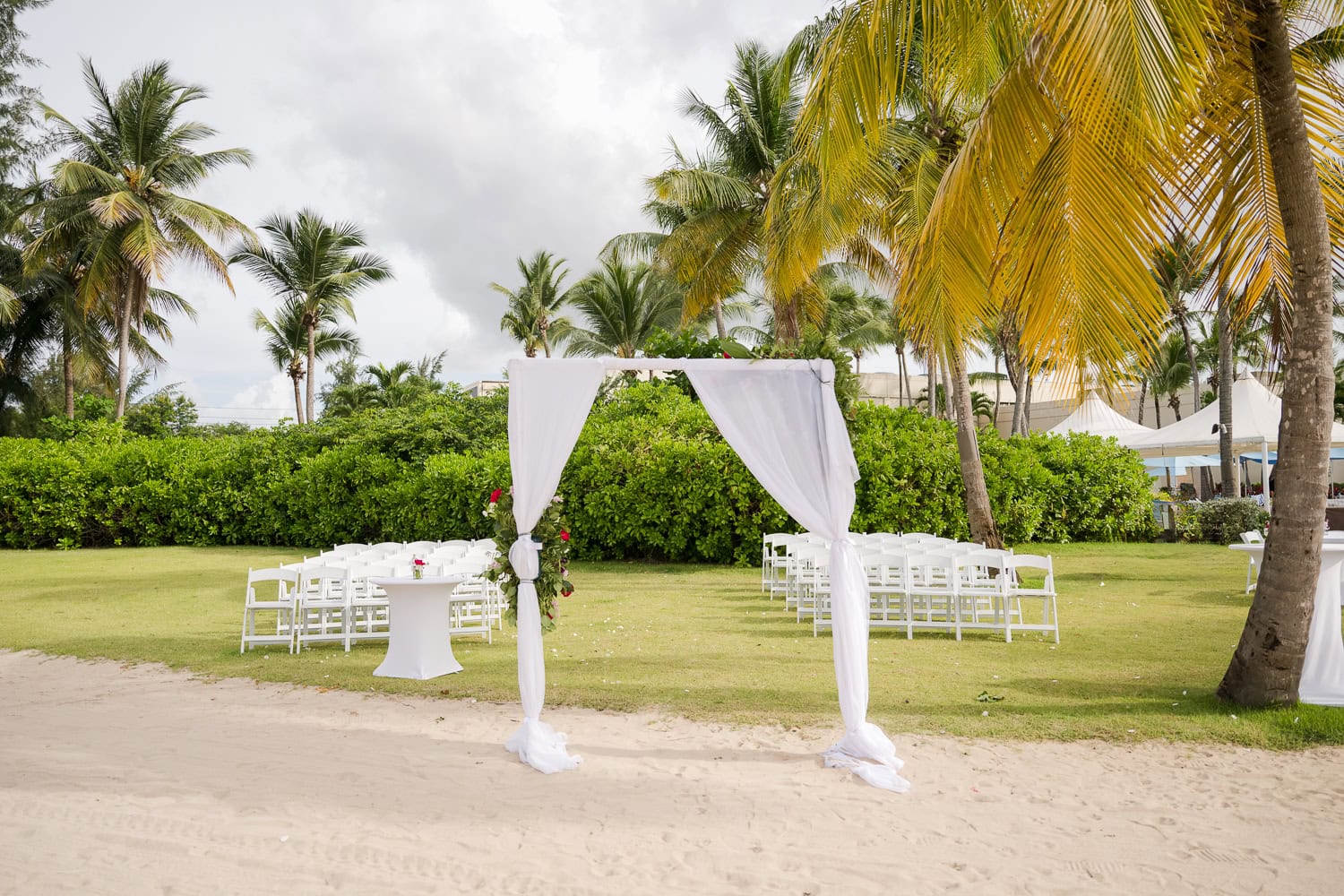 Beachfront wedding ceremony setup with a floral arch and palm trees at Courtyard Marriott Isla Verde, Puerto Rico.