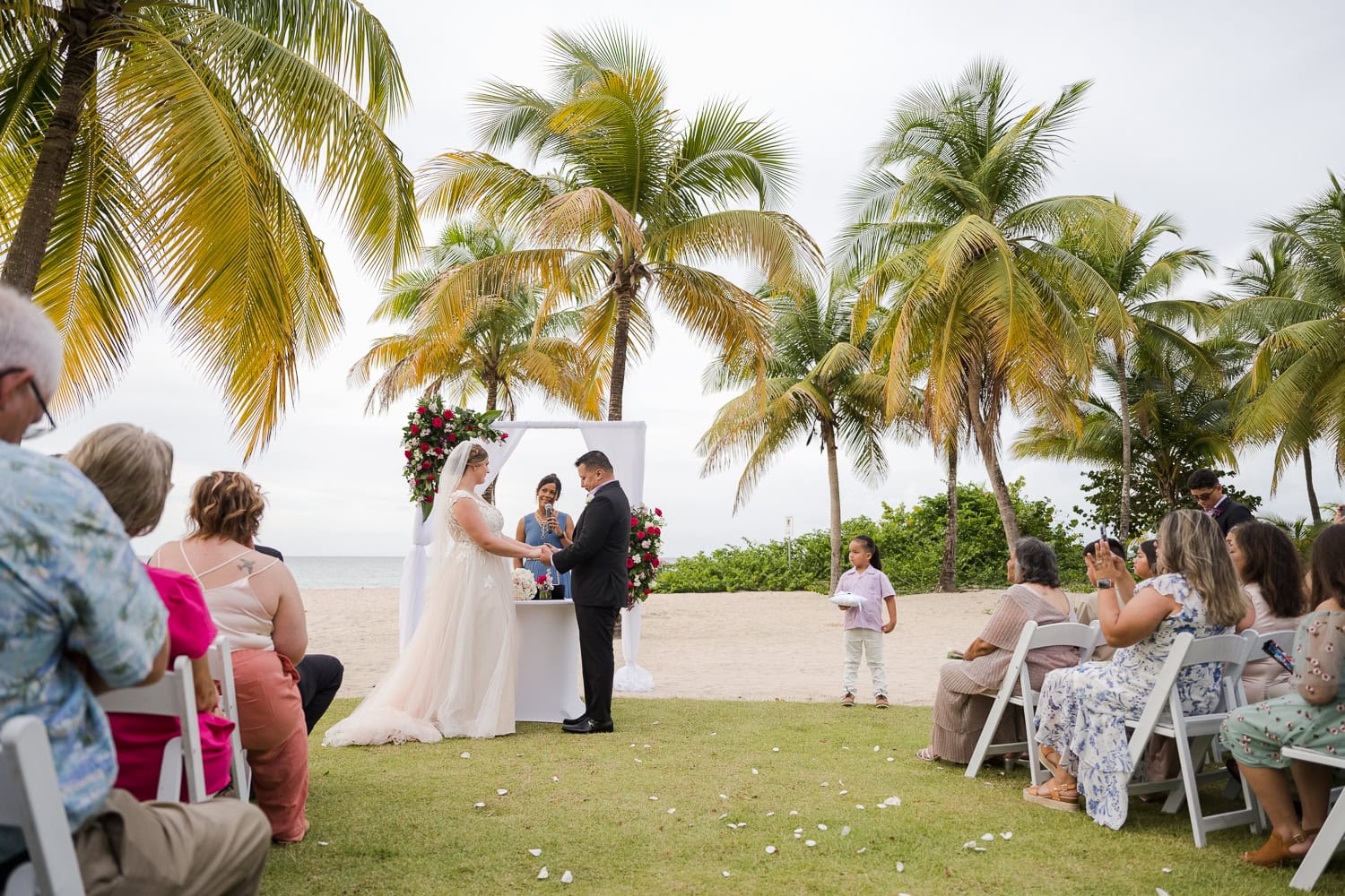 Beachfront wedding ceremony setup with a floral arch and palm trees at Courtyard Marriott Isla Verde, Puerto Rico.