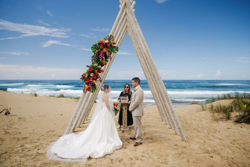 Bride and groom exchanging vows under bamboo tipi arch with tropical floral arrangement at Fusion Beach Villas, intimate beach wedding in Puerto Rico