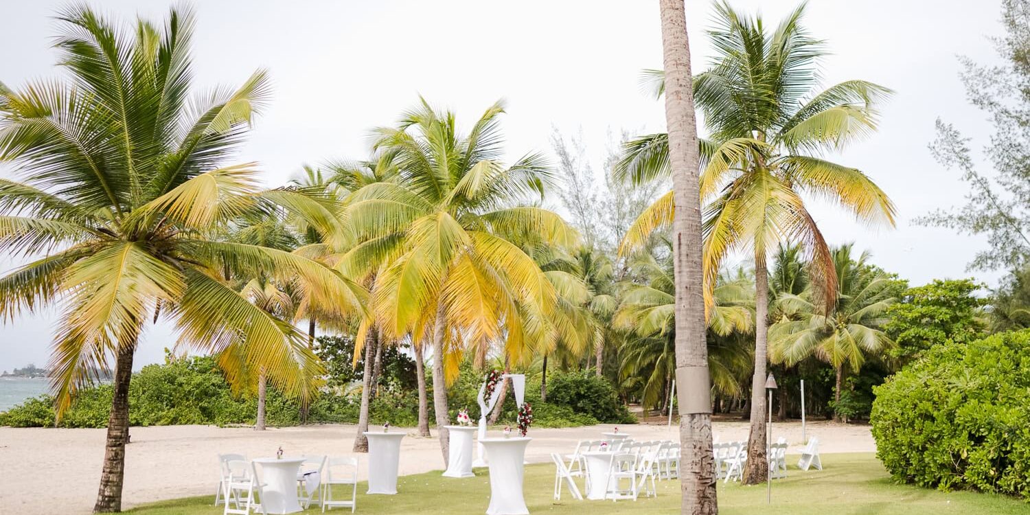 Beachfront wedding ceremony setup with white chairs and tropical floral arrangements at Courtyard by Marriott Isla Verde Beach Resort.